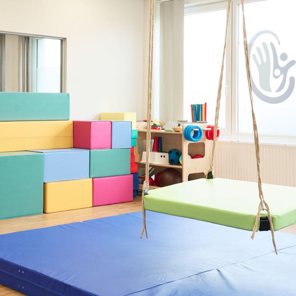 Therapieraum mit Schaukel, Matten und Bewegungsmaterialien.